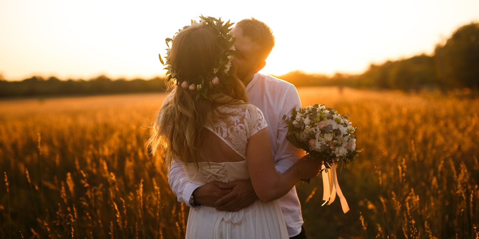 Bride and groom embracing in field during sunset