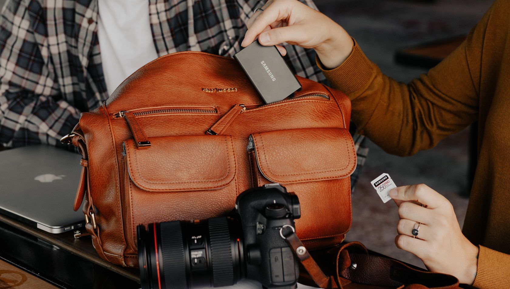 woman placing camera equipment into brown leather camera bag