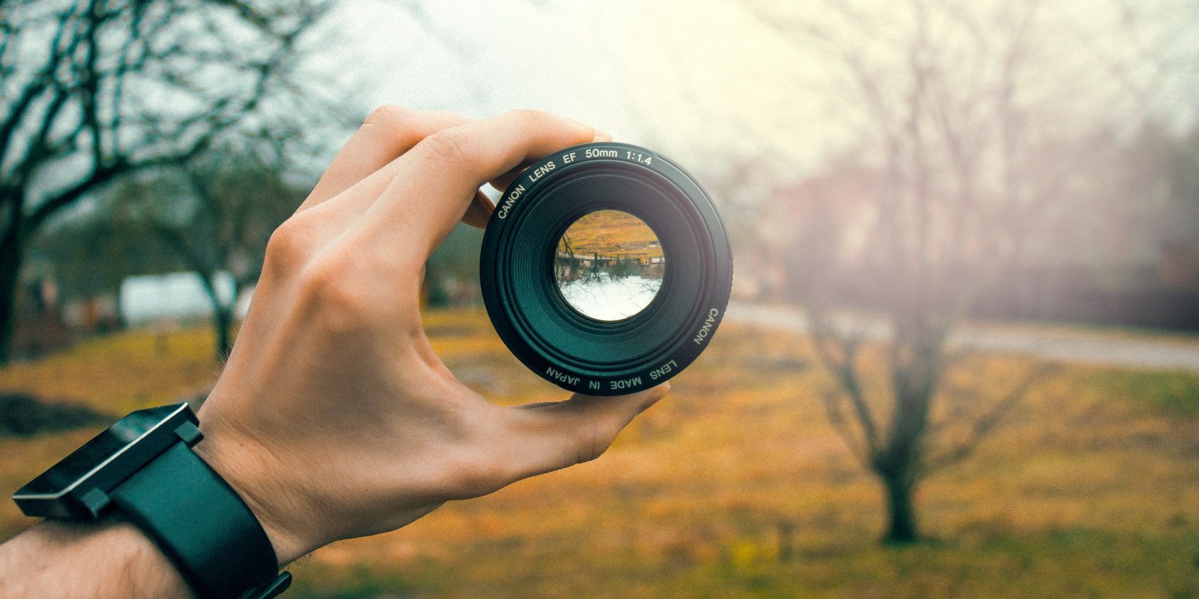 Person holding out camera lens with trees and sunlight in the background