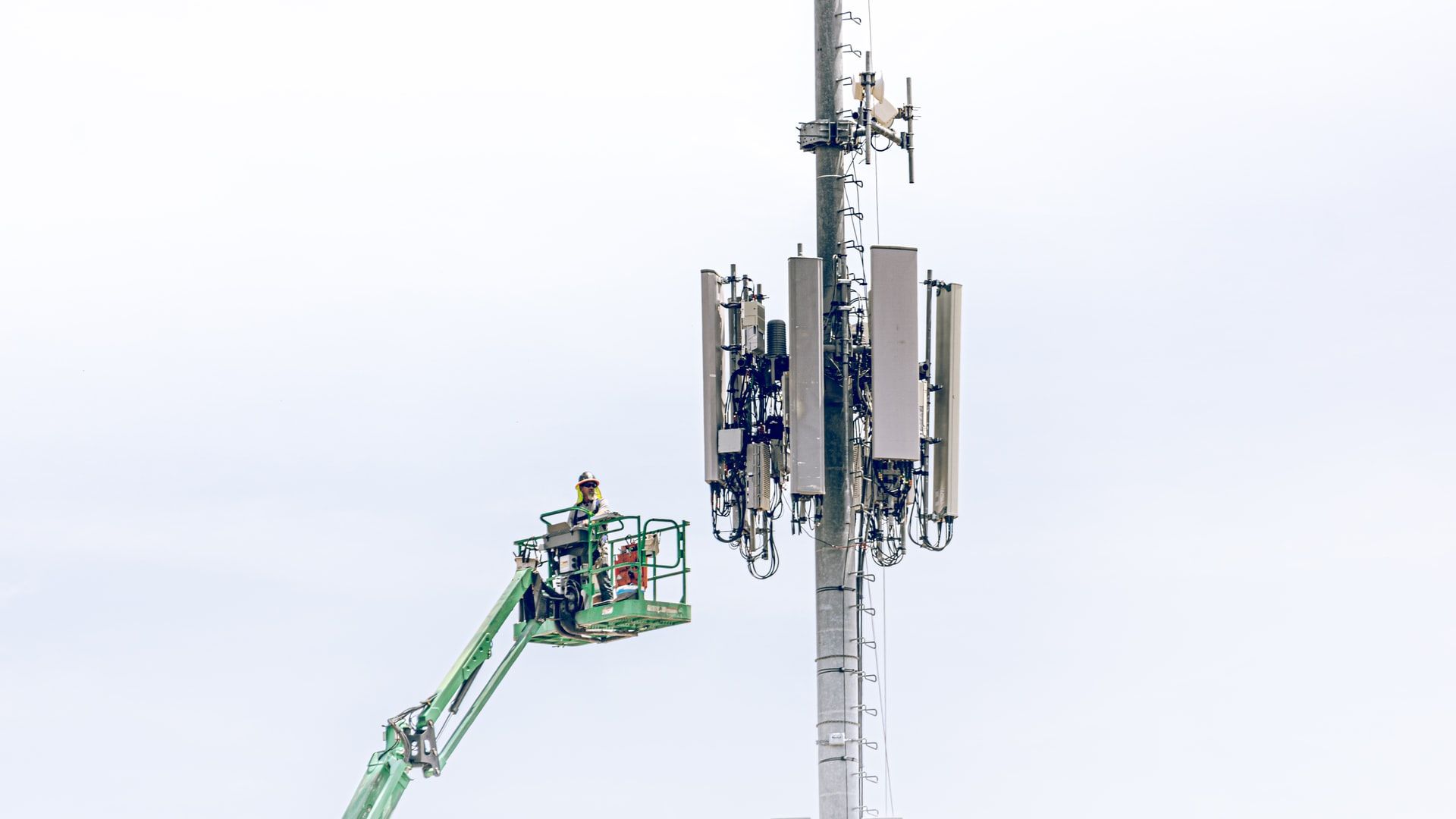 Image of a cell phone tower and a maintenance worker on a boom lift