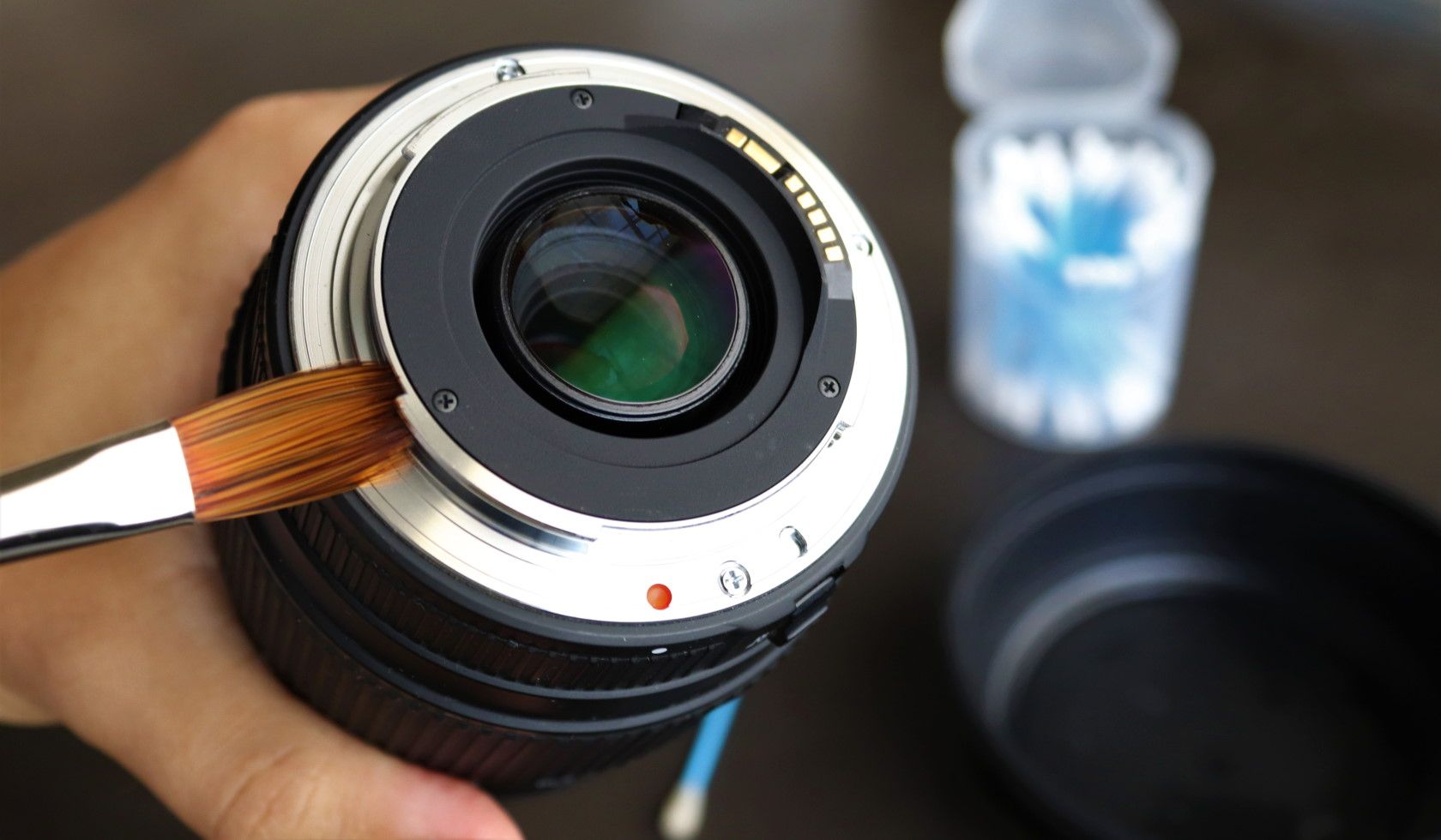 Close-up of person dusting camera lens with soft brush