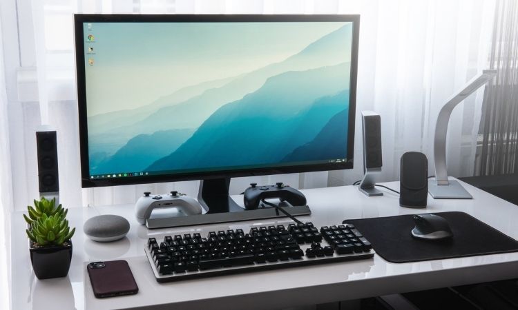 computer desktop workstation with bright lighting and a keyboard, two gaming controllers, and an ergonomic mouse