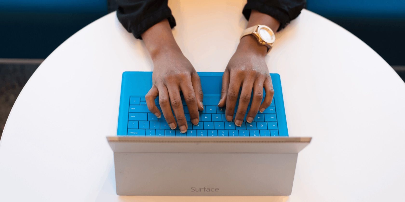 Hands typing on the vivd blue keyboard of a Surface tablet