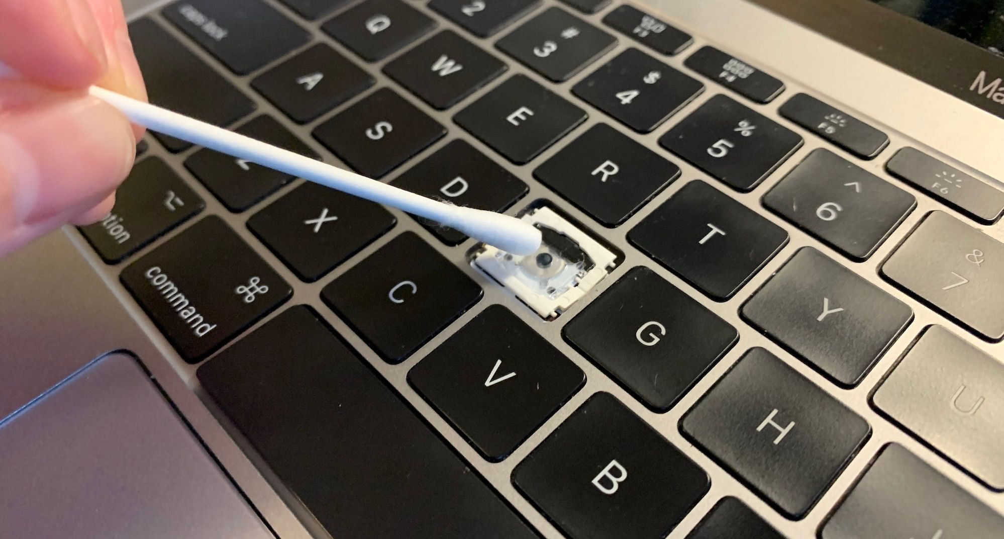 A hand cleaning undeneath where a macbook keycap usually attaches, using a cotton swab