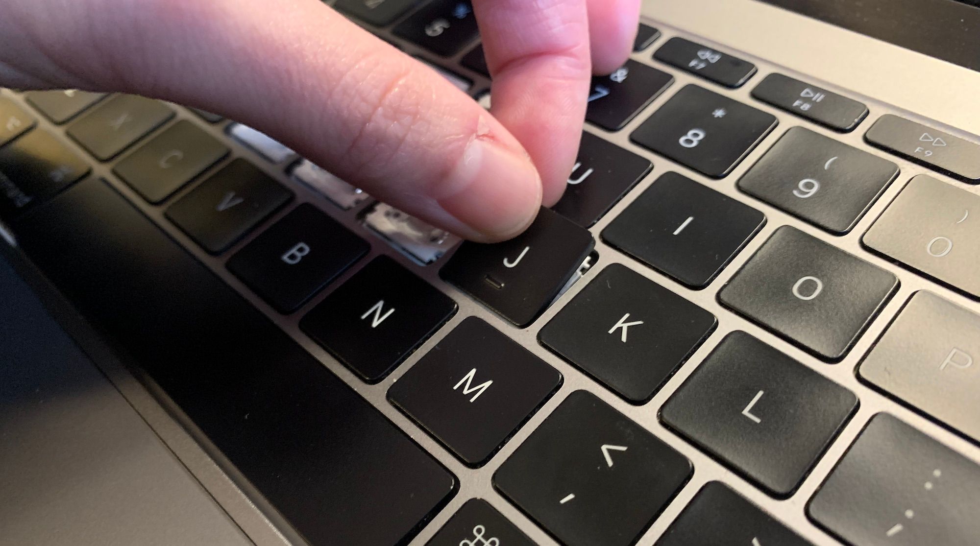 A hand re-attaching a macbook keycap in its original place