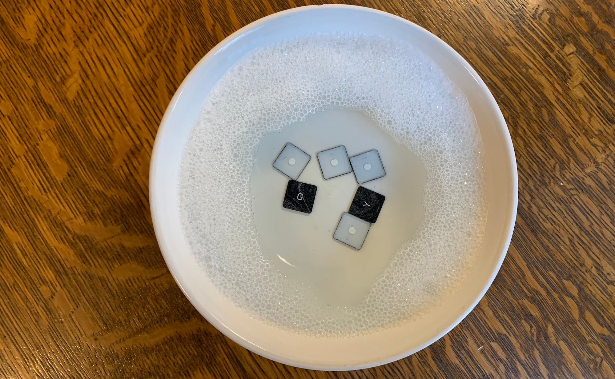 A top down shot of macbook keycaps in a bowl of soapy water