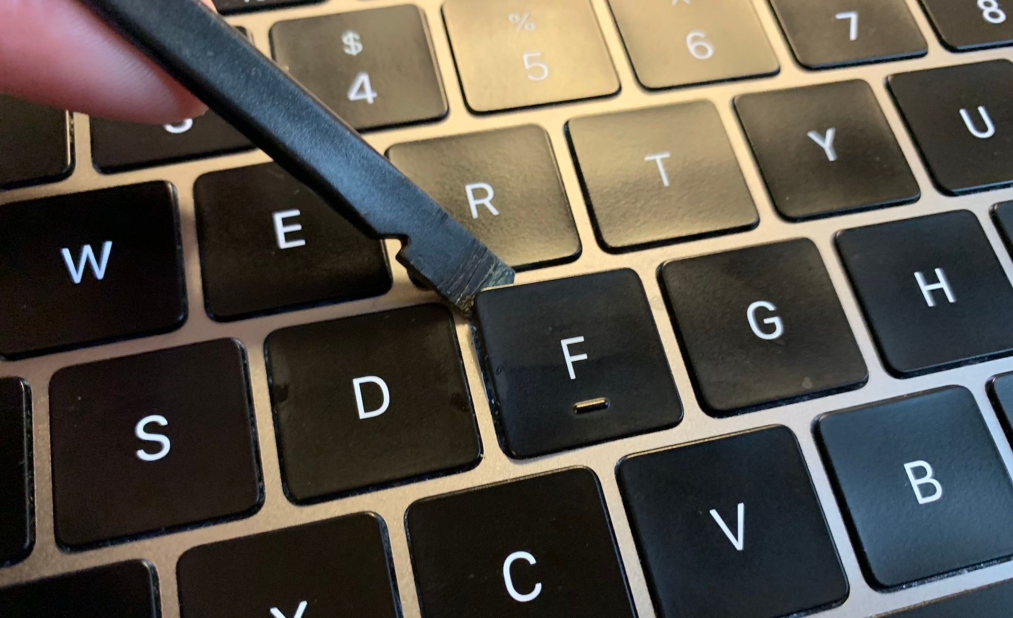 A close up shot showing a spudger tool under the left corner of a macbook key cap