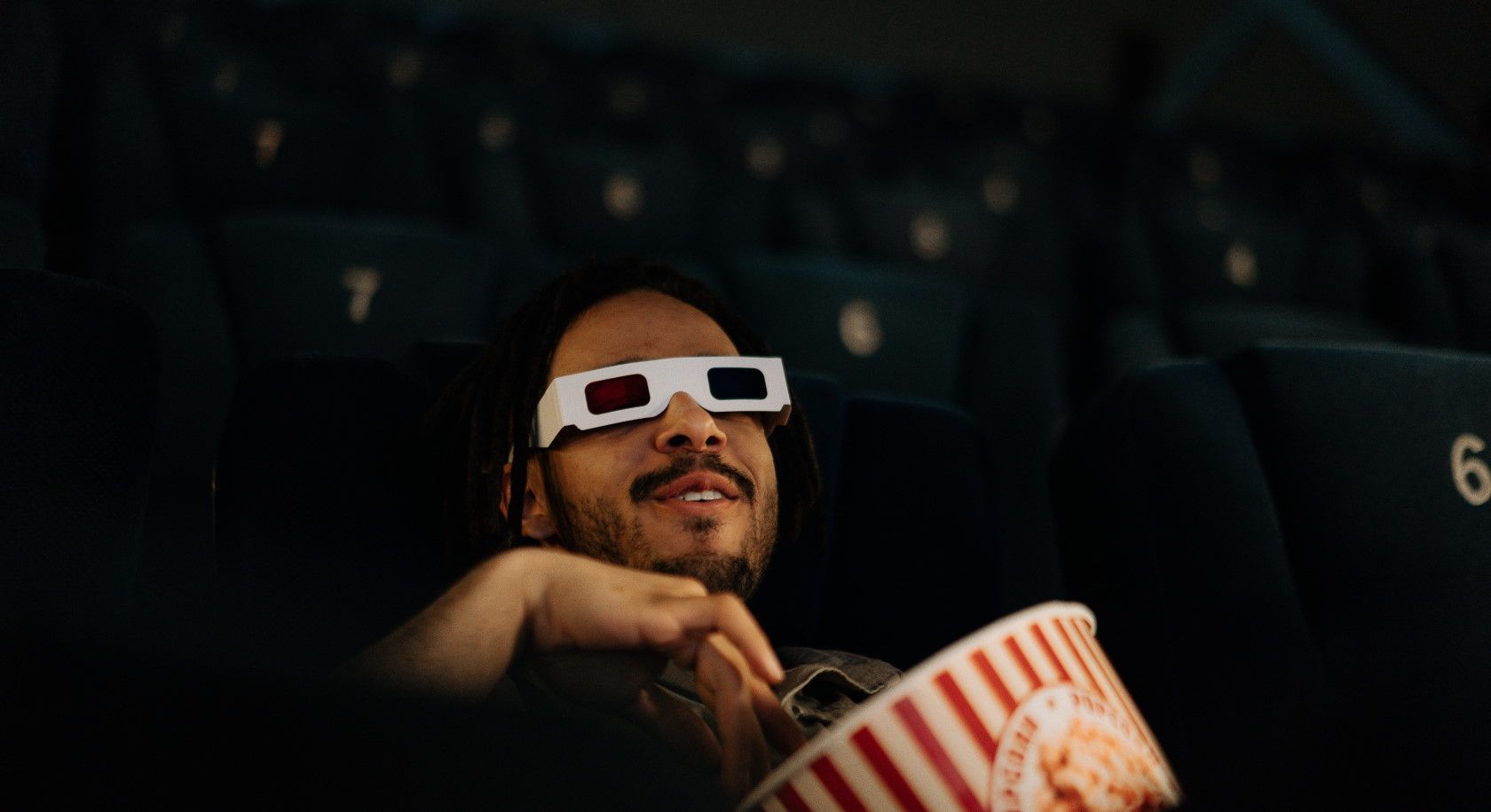 Man laughing in movie theater and eating popcorn wearing 3D glasses