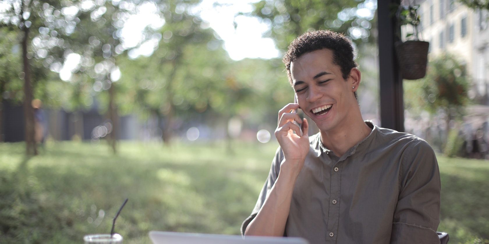 A man using a laptop while smiling as he talks on the phone.