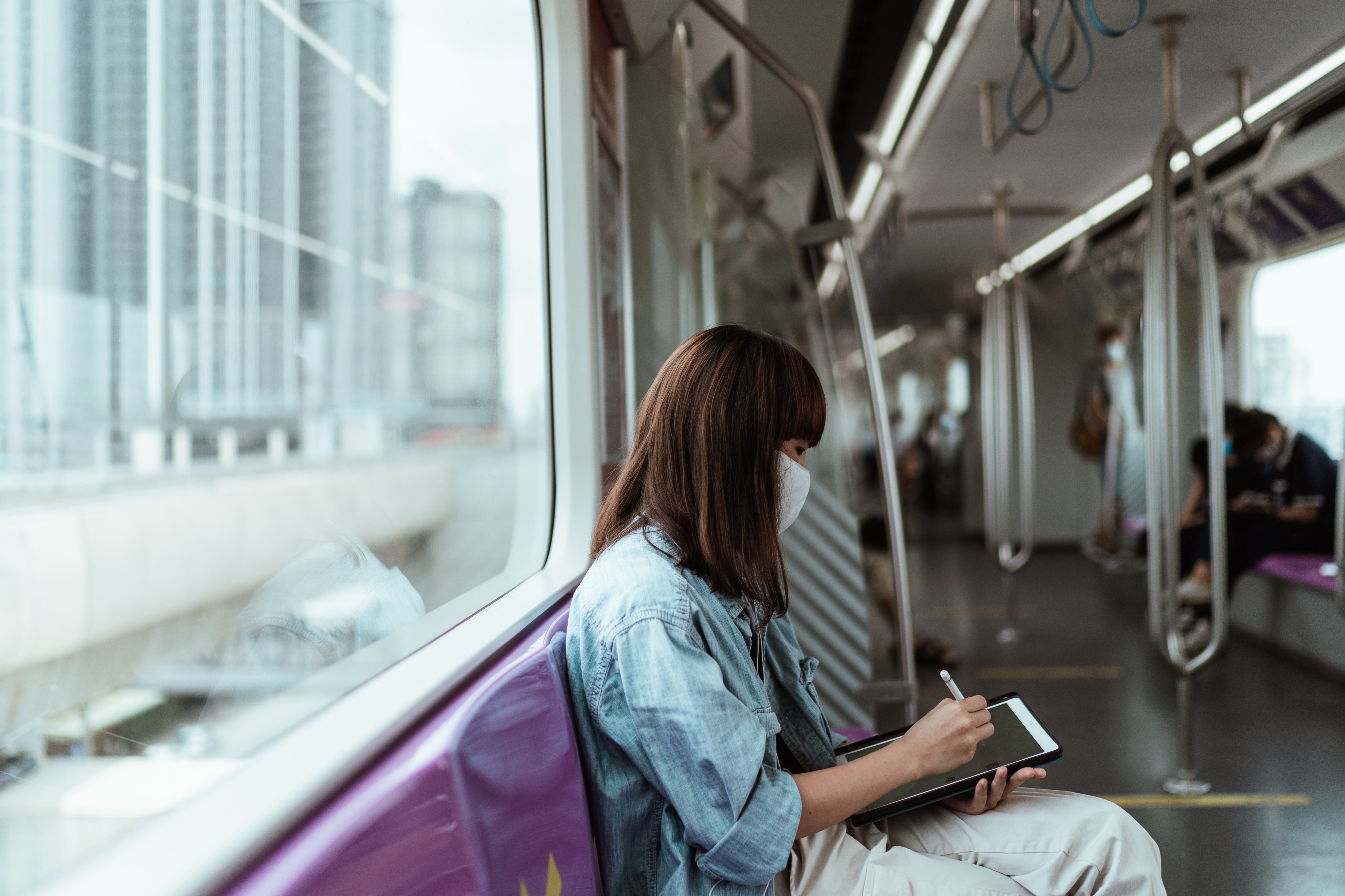 A woman wearing mast writing on her tab in train