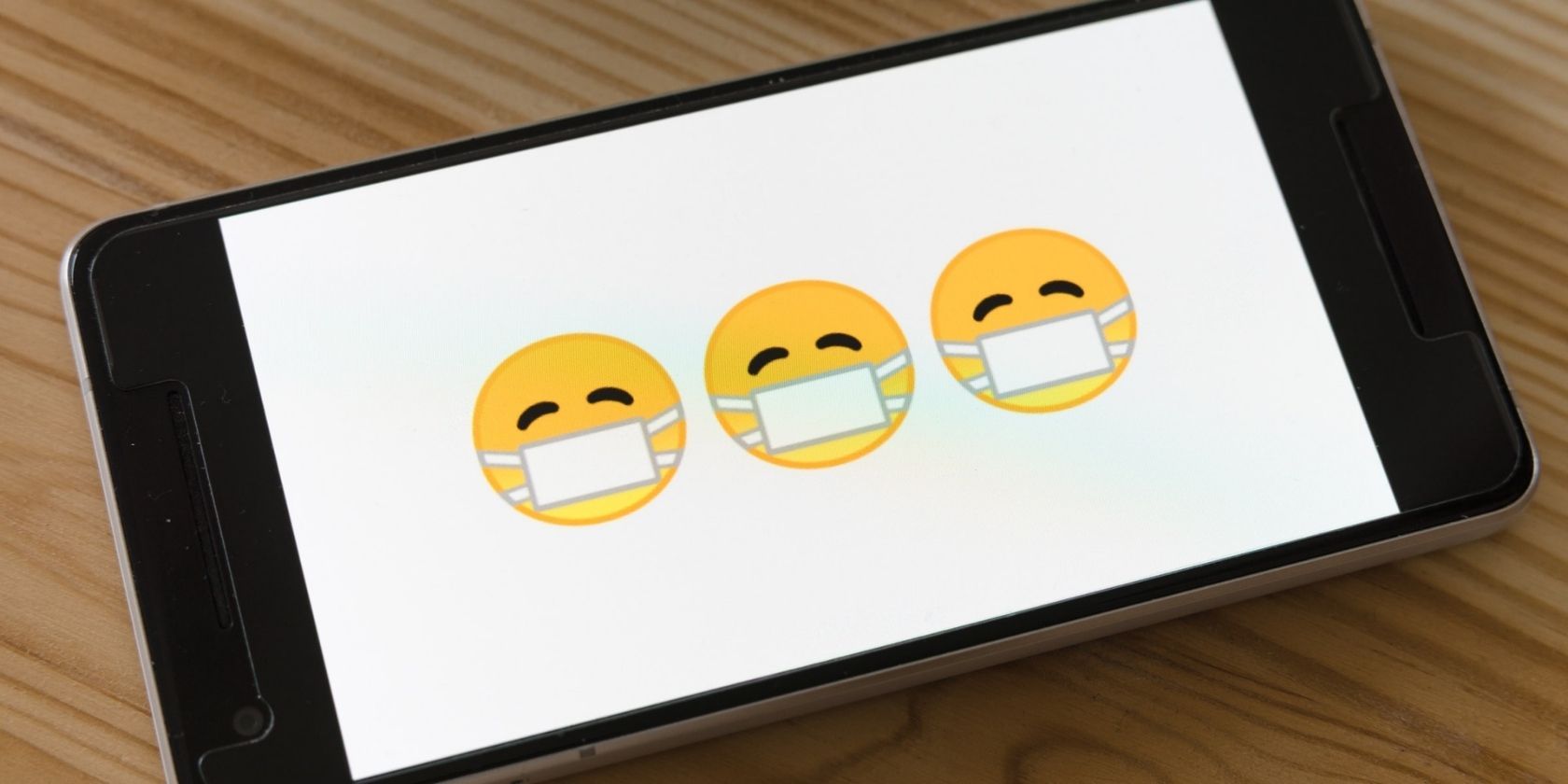black phone laying faceup on wooden table with three masked emojis on the screen