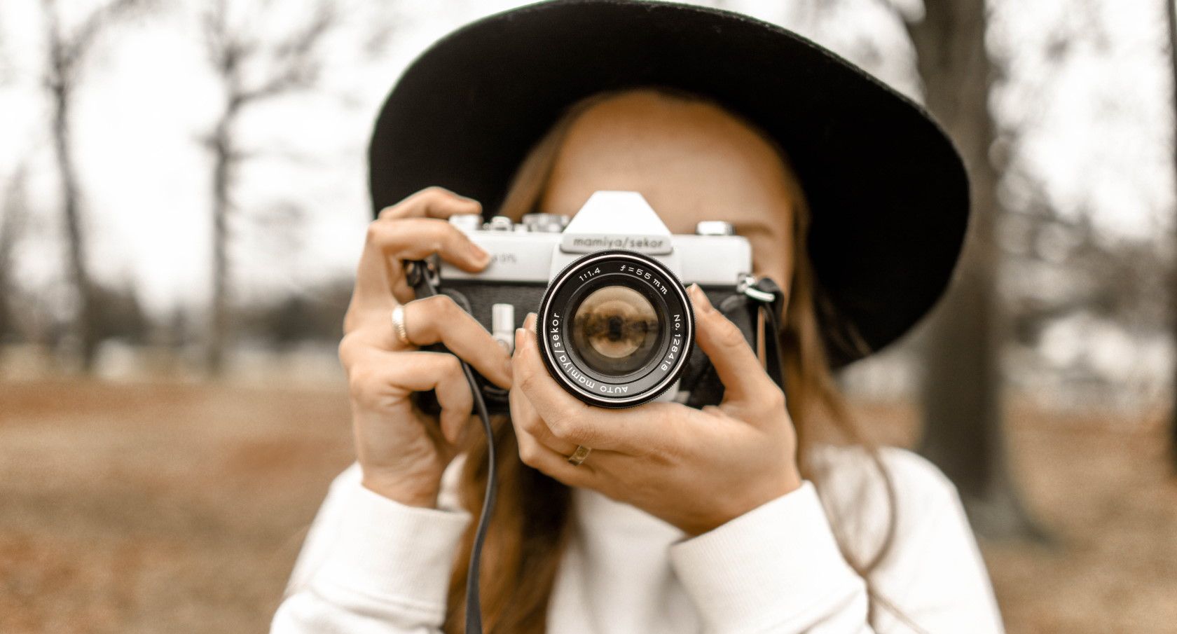 Woman wearing hat taking photograph using vintage camera