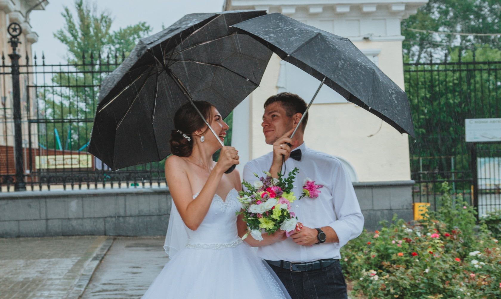 bride and groom standing outside holding umbrellas in the rain