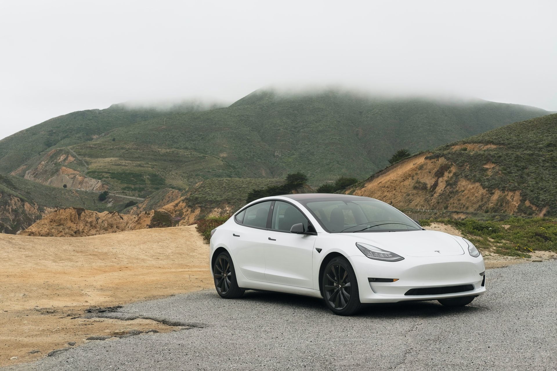white tesla model 3 with black wheels with mountains in background
