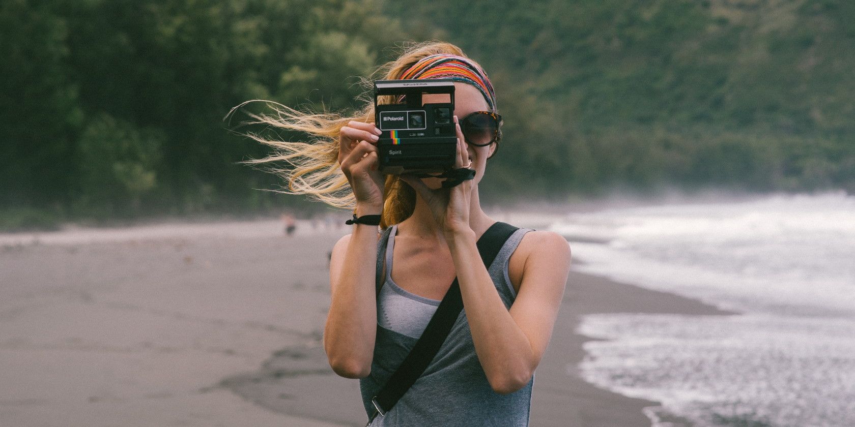 Woman standing in the wind on the beach holding camera