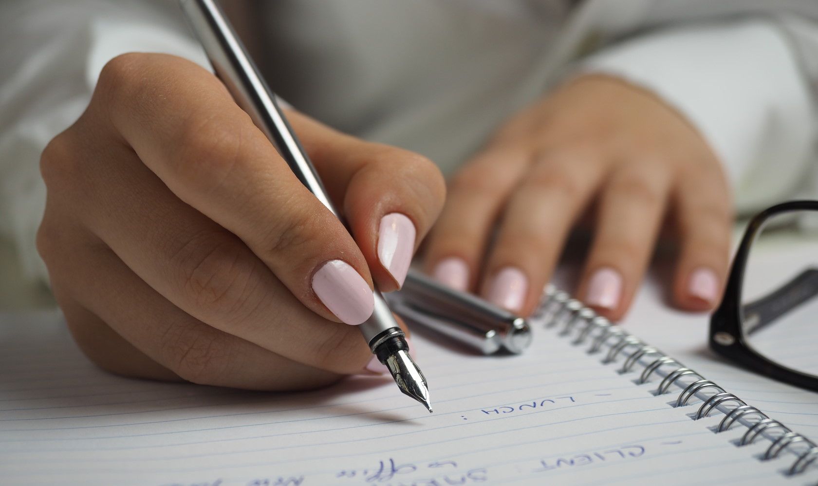 Woman with pink painted nails writing down notes on writing pad