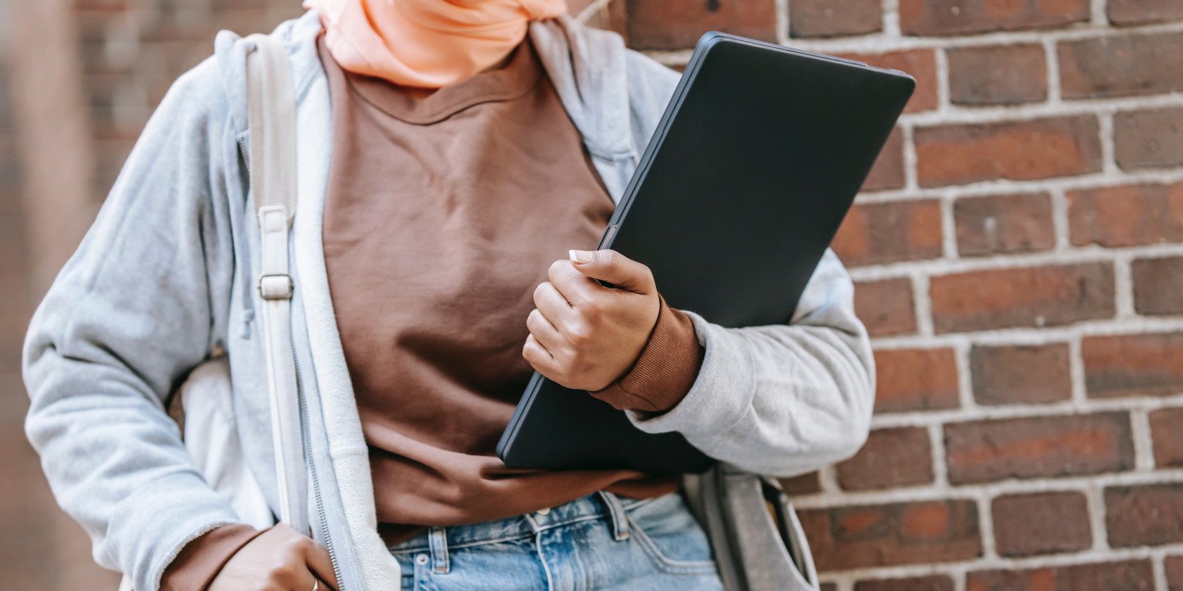 Woman holding laptop near brick wall on street