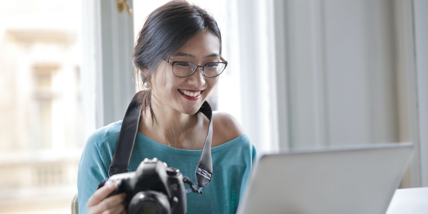 Image shows a woman with a camera smiling at a laptop