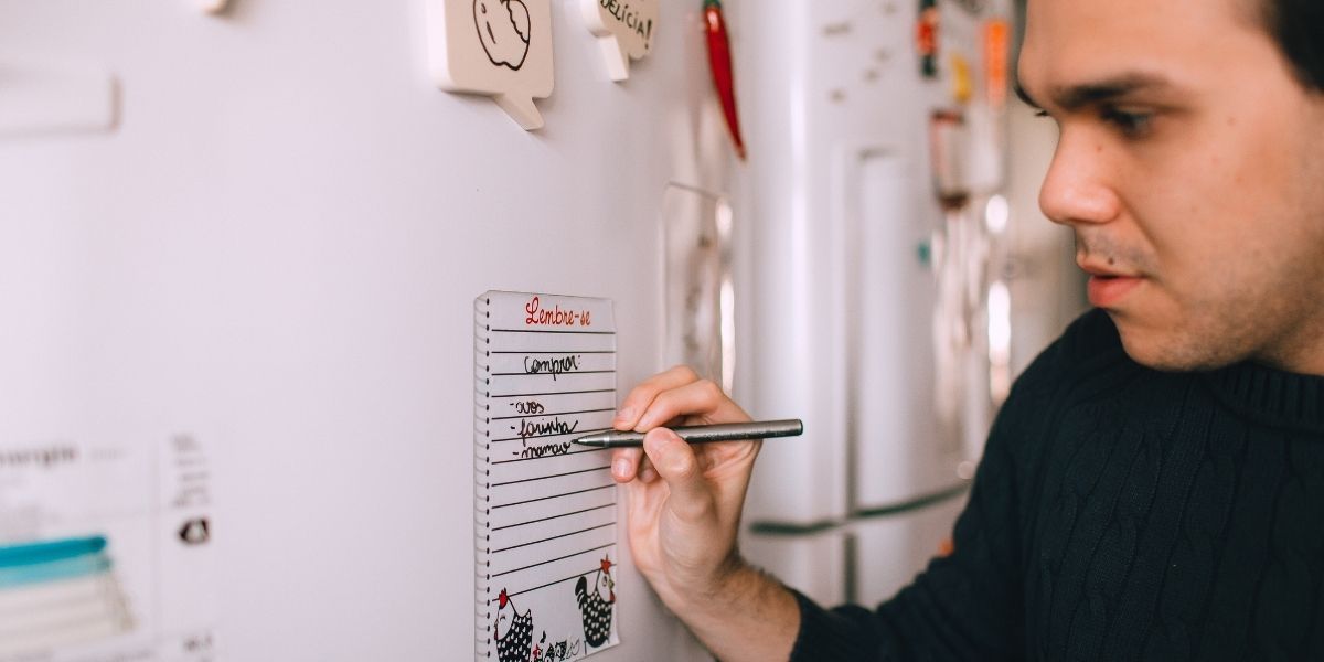 Young man writing reminder on fridge note