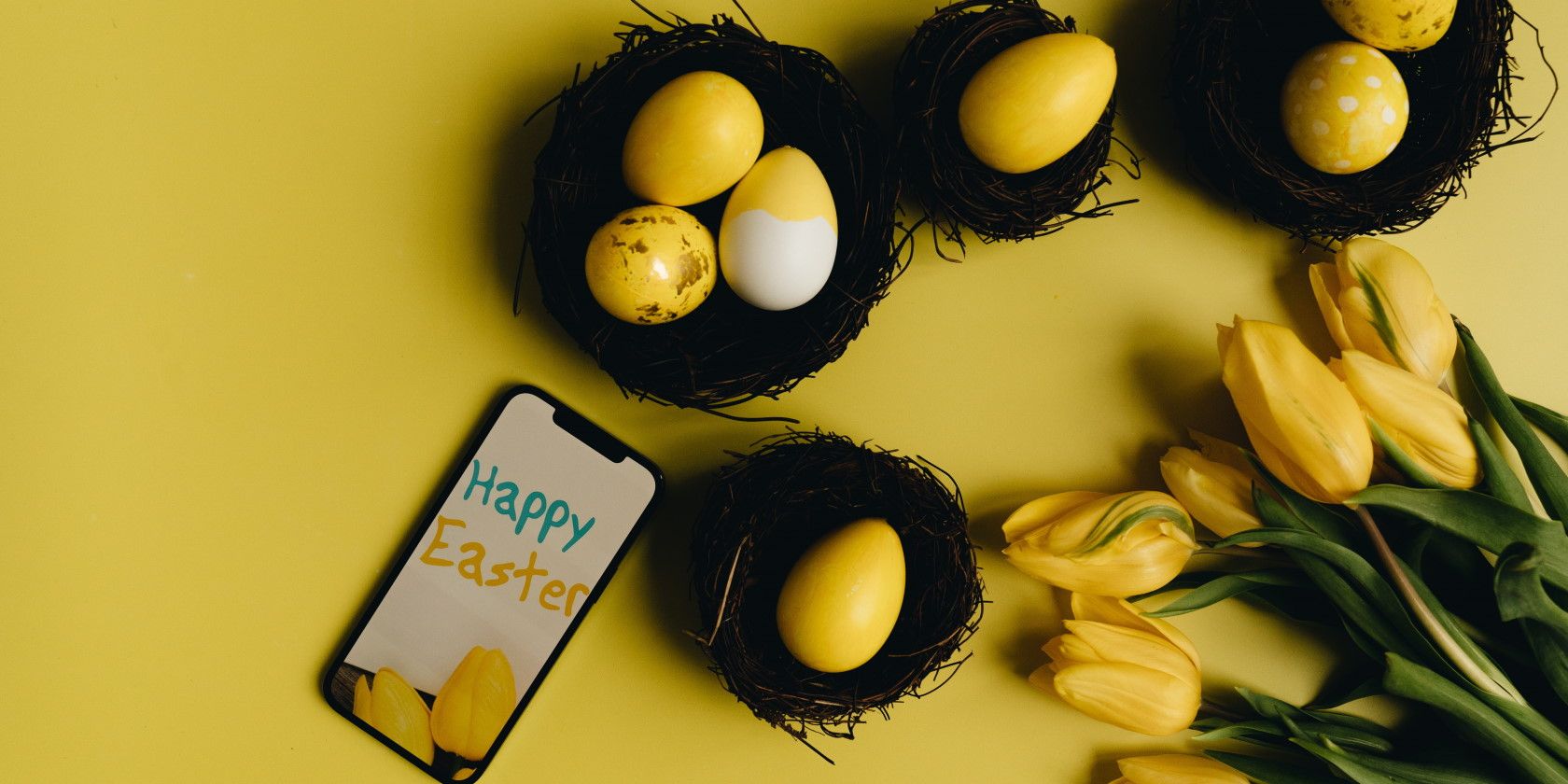 Smartphone with Happy Easter message alongside yellow Easter eggs and flowers