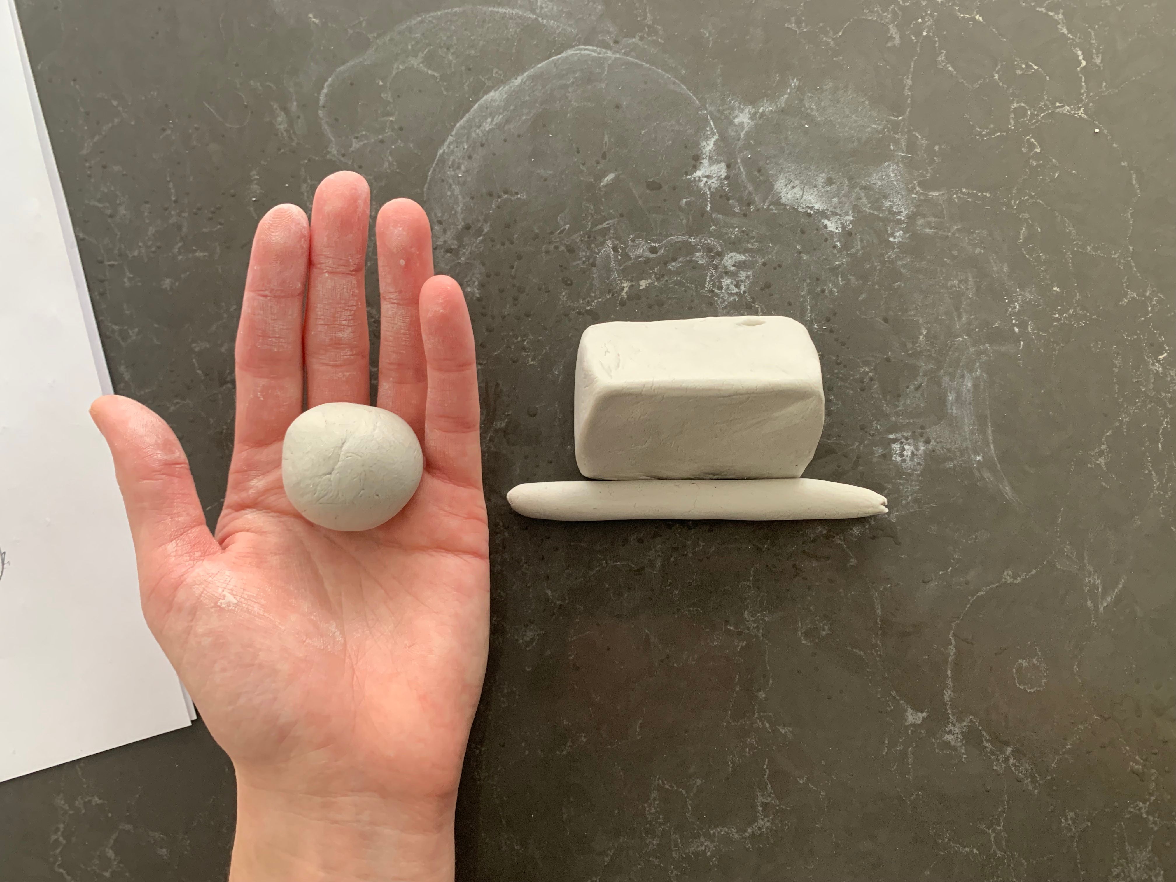 A hand holding a ball of clay next to a clay triangle and thin cyclinder shape