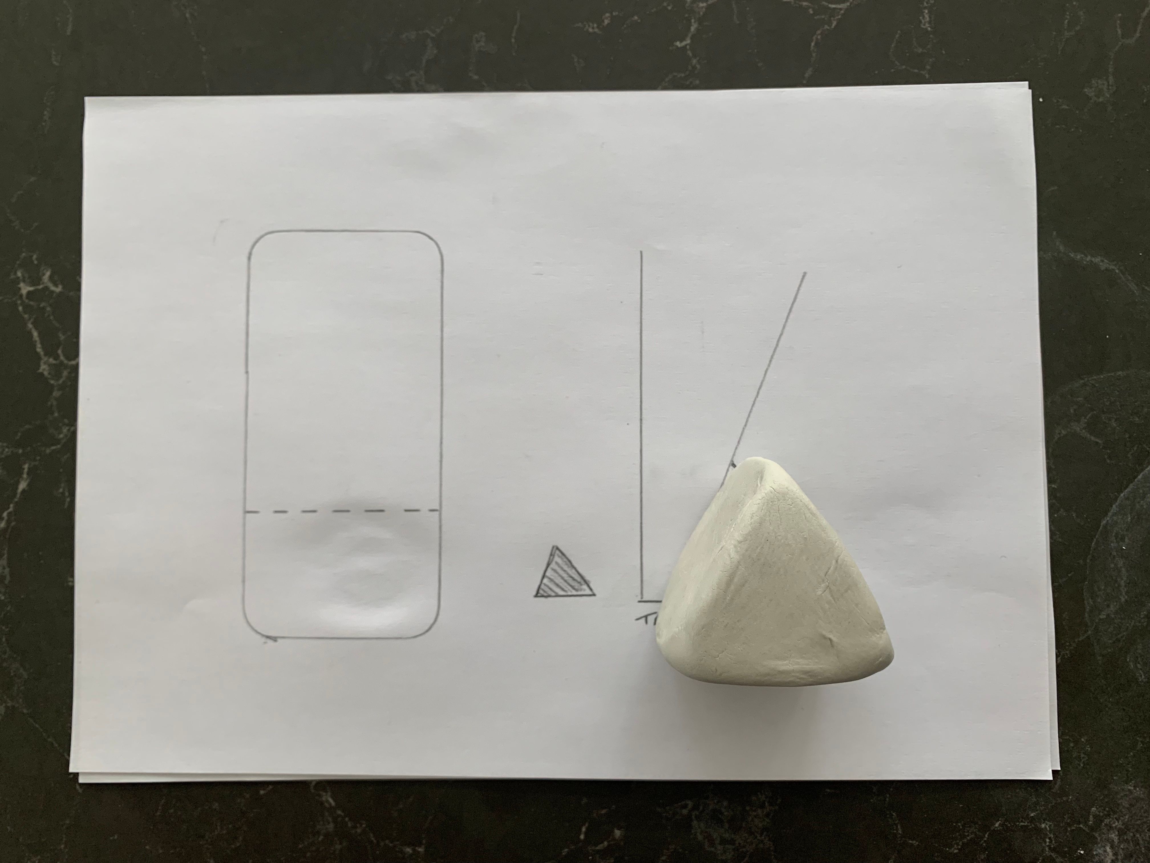 A triangle shaped piece of clay compared against the phone outline on paper