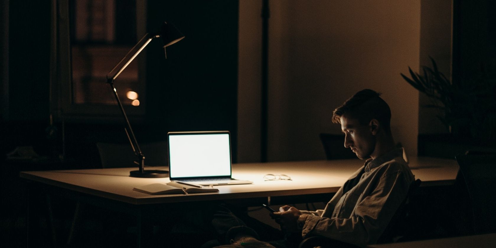 MacBook sitting on desk in dark room with man looking at phone