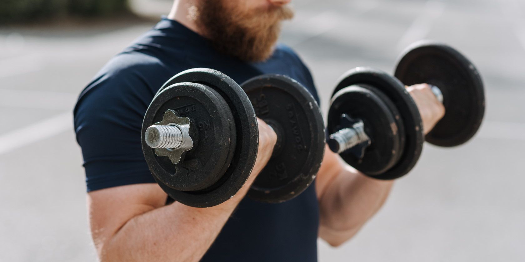 Man exercising outside and lifting two black dumbbells