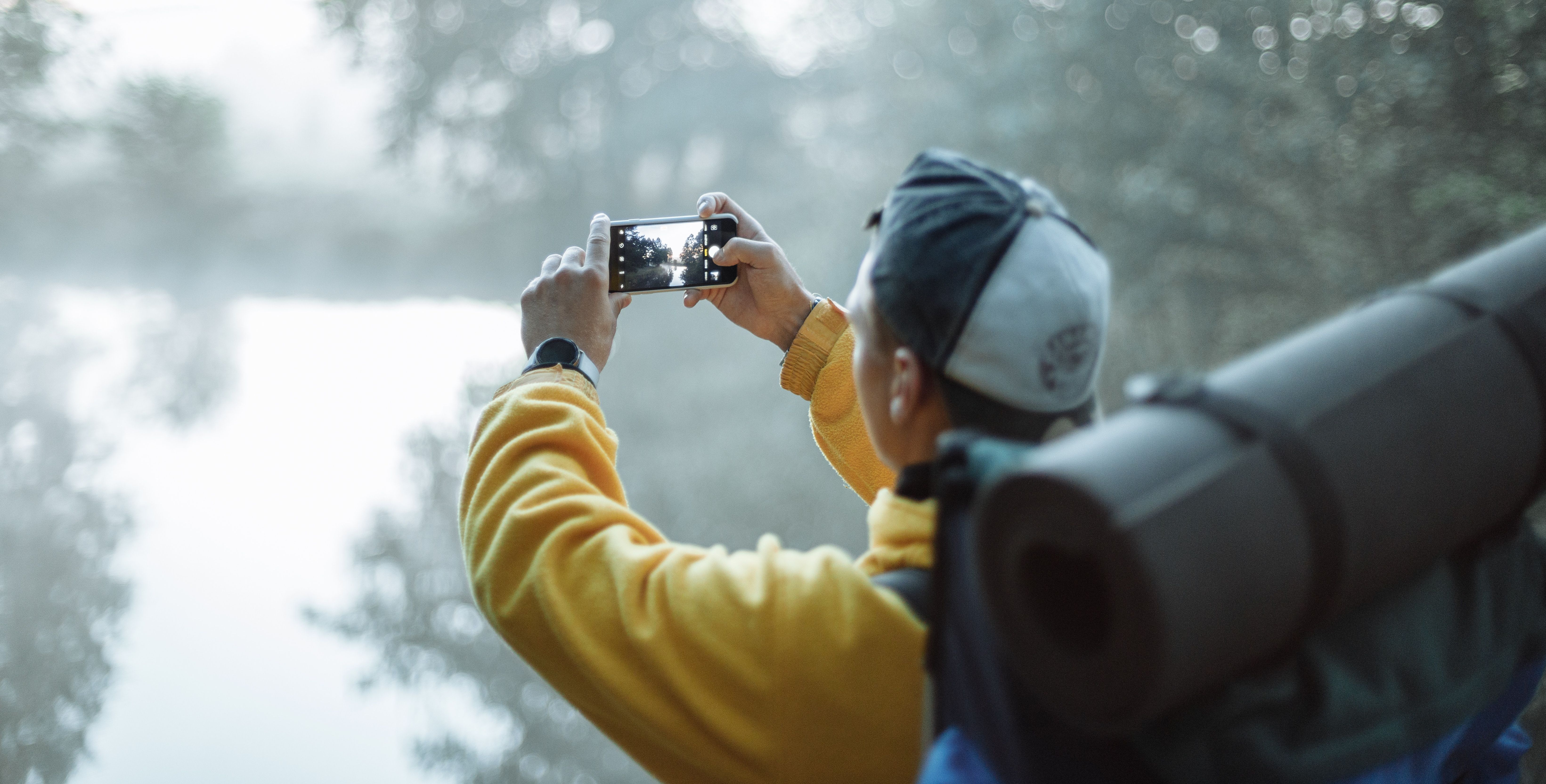man using smartphone to take photo of lake
