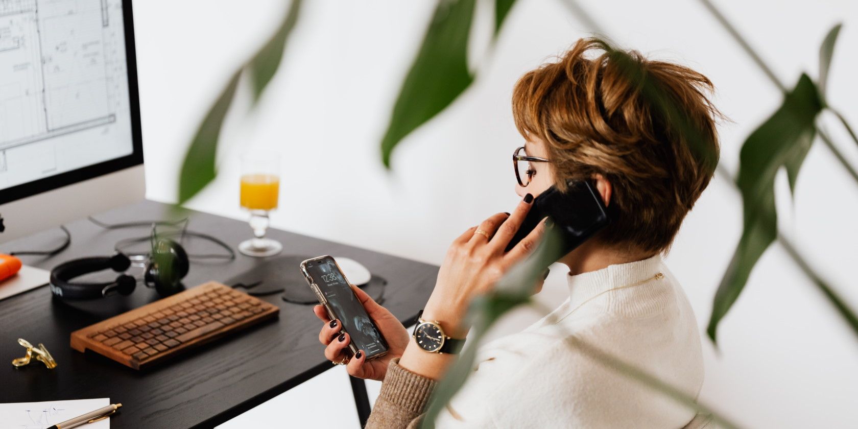 Woman sitting at desk in front of computer and using multiple phones