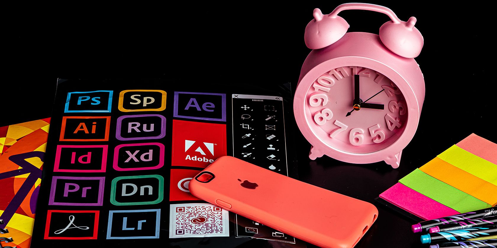 Adobe product logos and a pink alarm clock, red iPhone, and colored post-its.