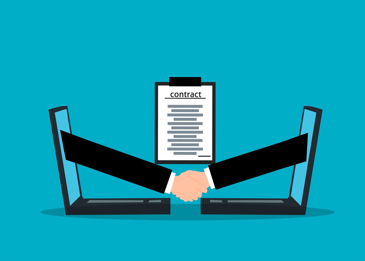 Concept Image of Virtual Contract Agreement depicting a handshake between two computers with a contract agreement in the background.