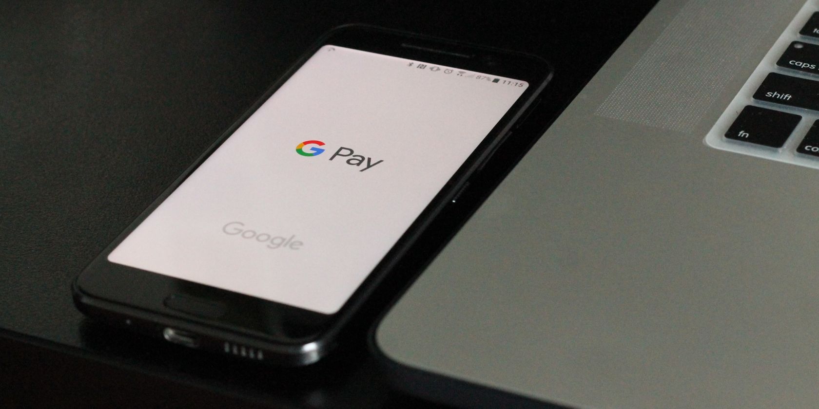 An unlocked phone with the Google Pay app open, next to a laptop.