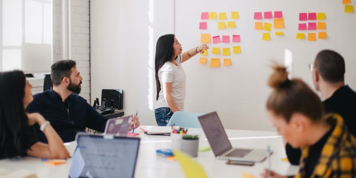 woman placing sticky notes on white wall in meeting with four people