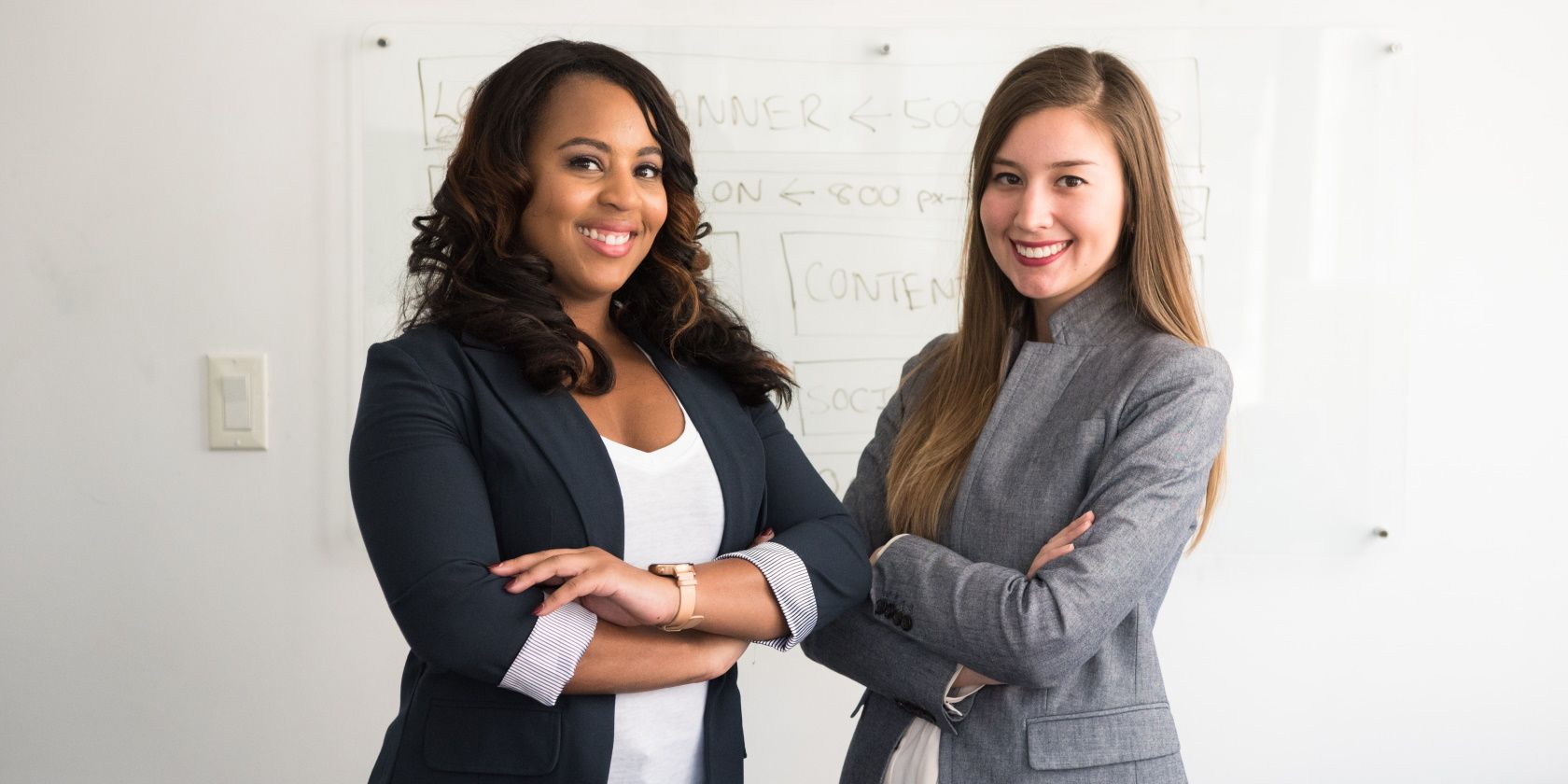 Two Businesswomen Arms Crossed in Front of Whiteboard