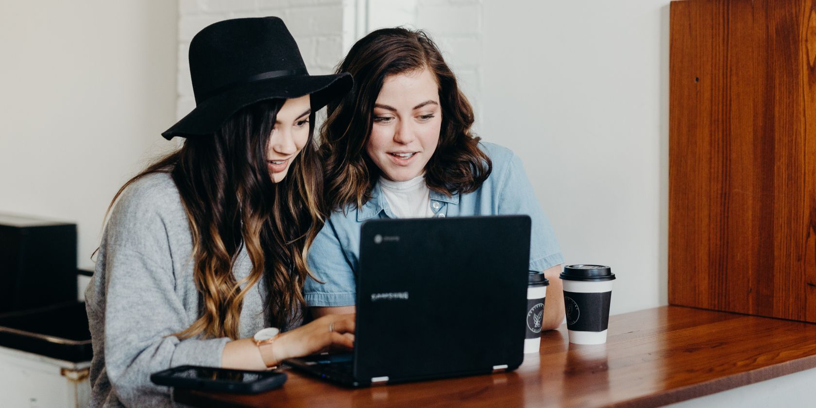 Two women using laptop and drinking coffee