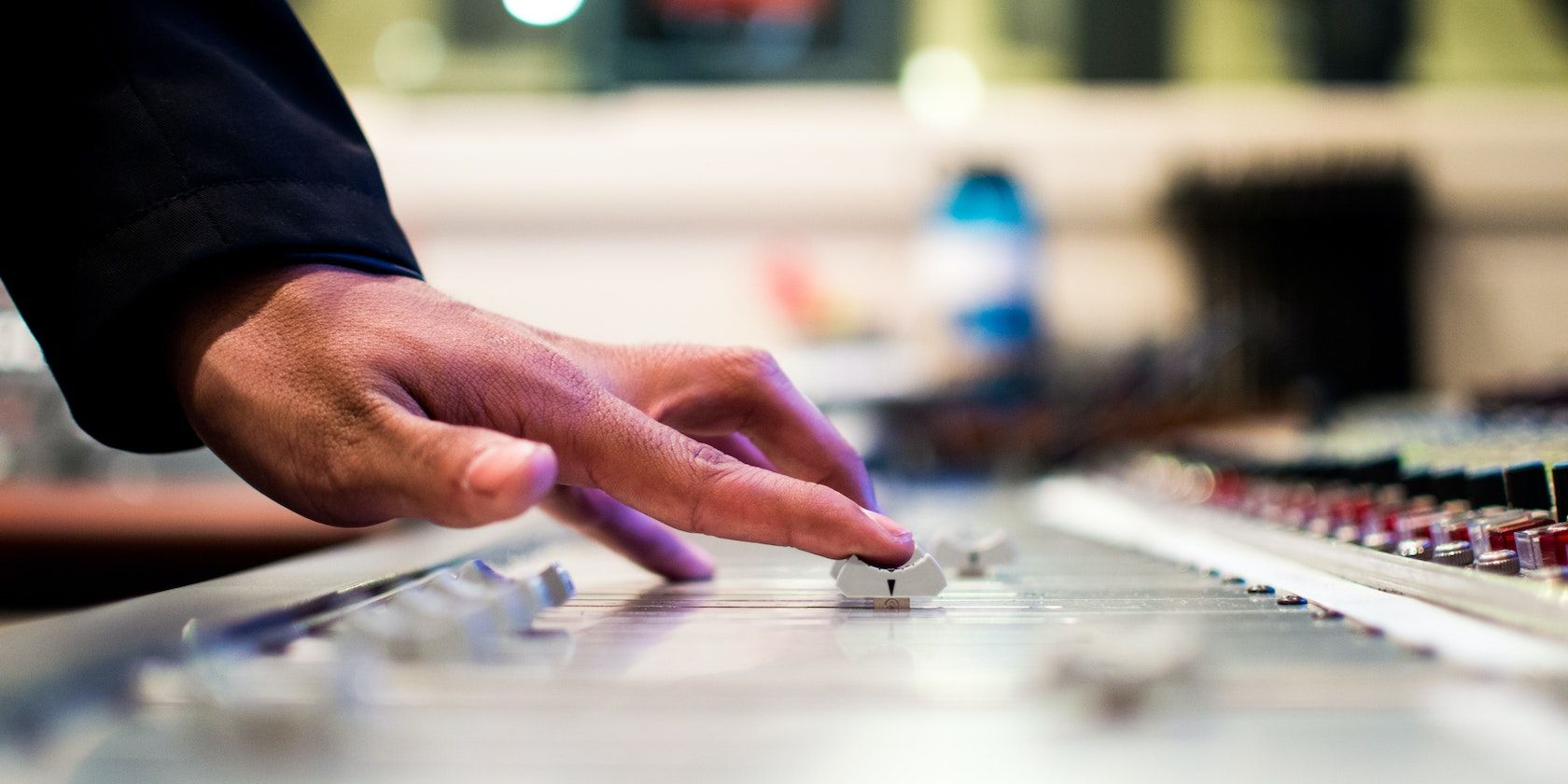 A close up photo of a hand pushing a fader on an audio mixer console