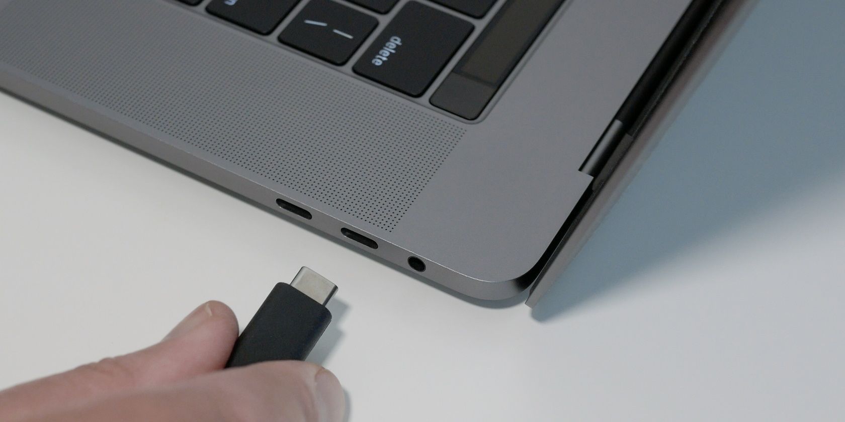 Man's hand plugging in a black USB Type C cable into the USB-C port on a laptop or notebook computer.