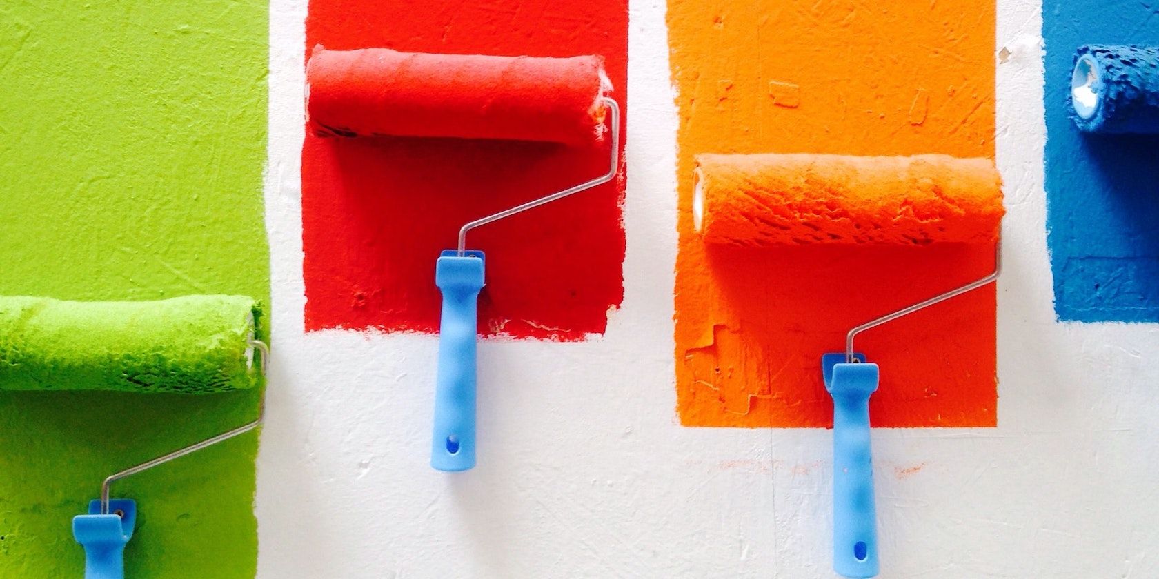 Four rollers paint colorful blocks onto a wall in green, red, orange, and blue