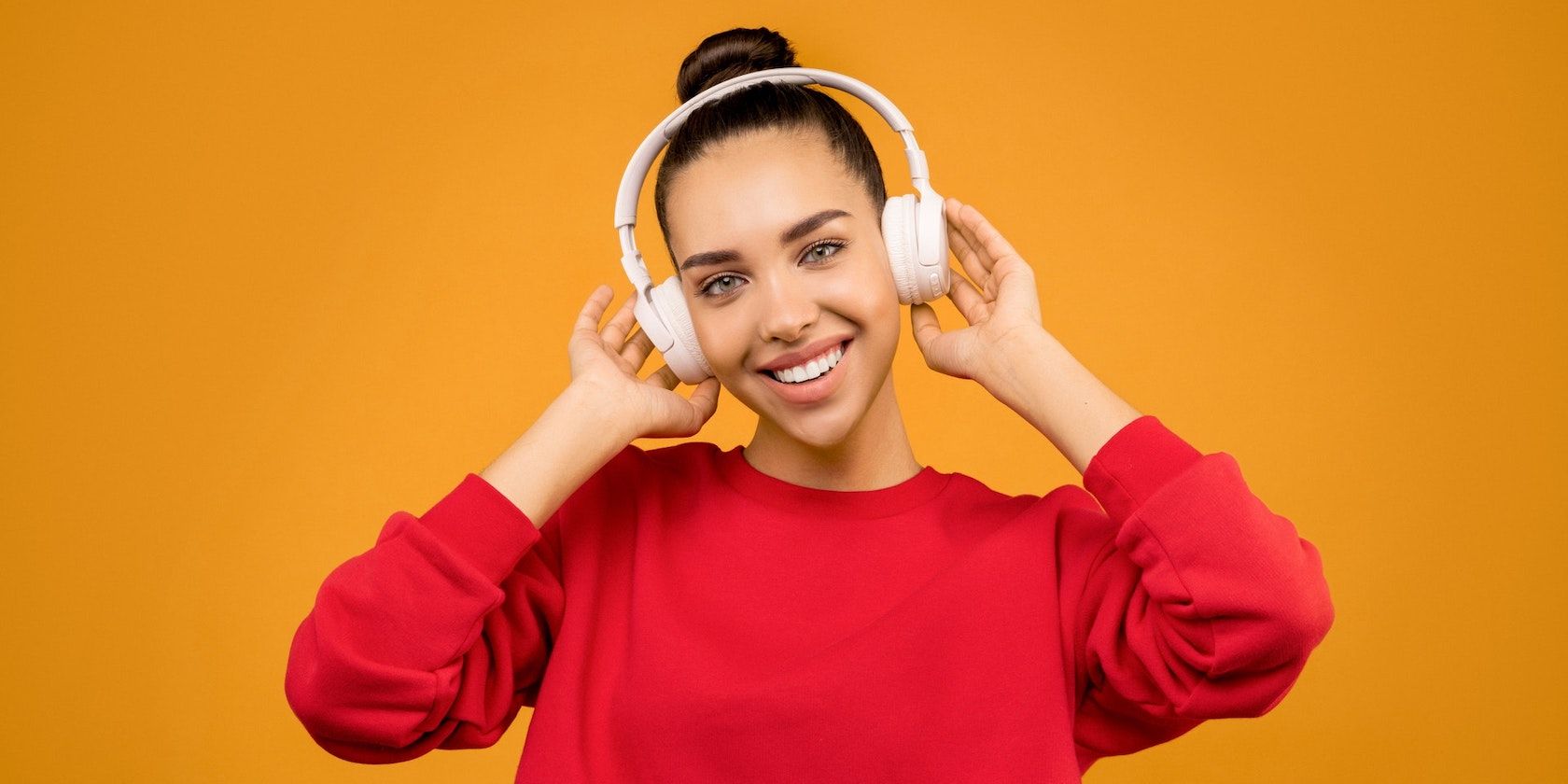A woman wearing headphones against an orange background