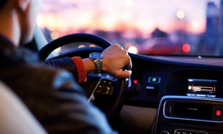 man with a watch and black jacket driving a car at sunset