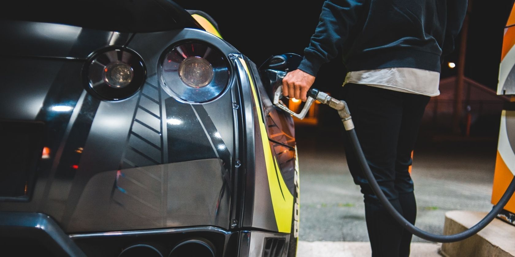 man in a blue jacket pumping gas in a black car with yellow stripe