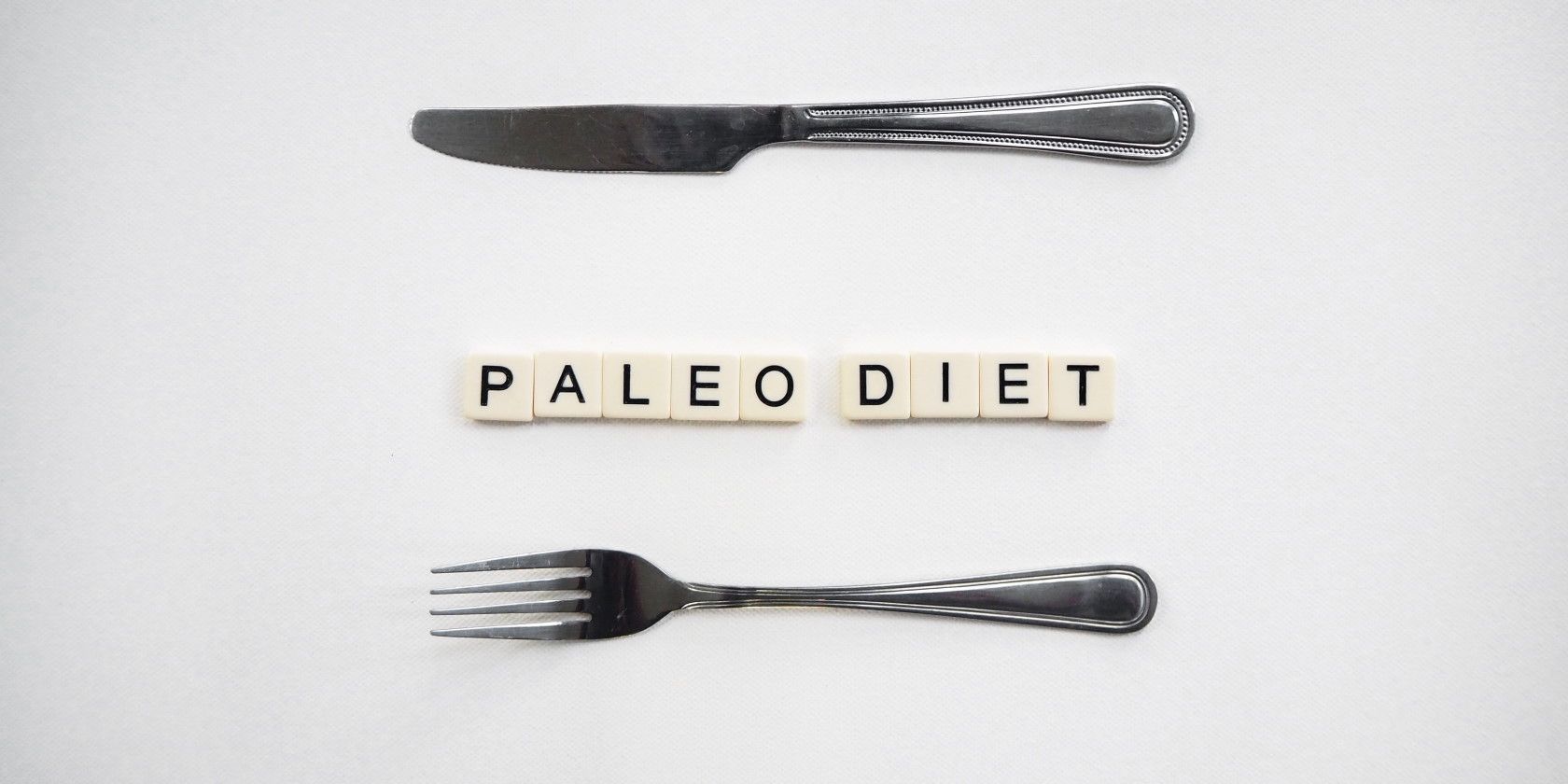 knife and fork on tabletop next to tiles spelling out paleo diet