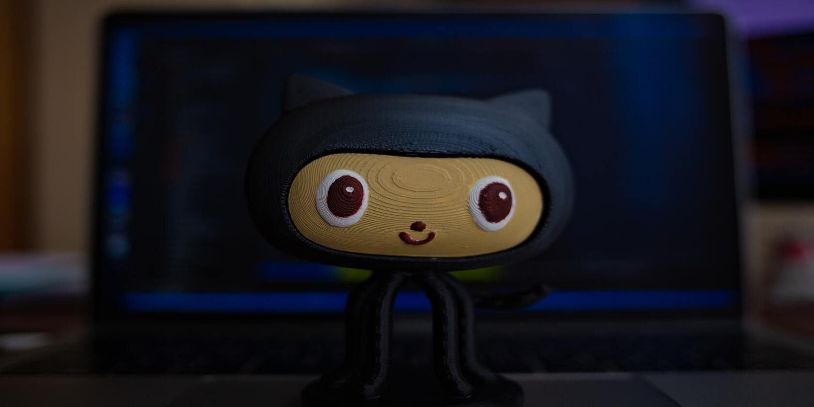 GitHub octocat plush toy in front of a blurred terminal