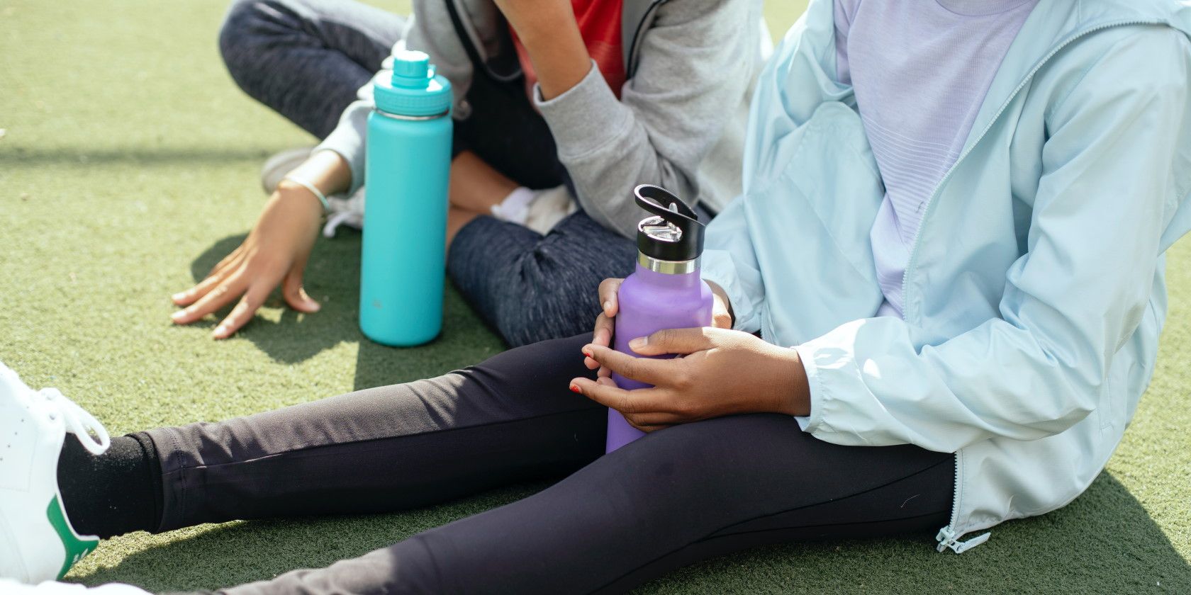 Close-up of teenagers sitting down with water bottles after exercising