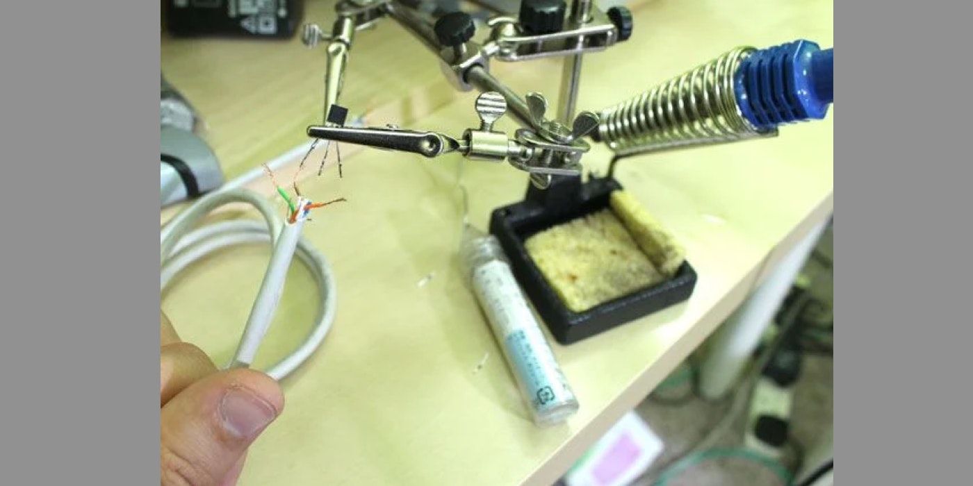 A hand holding an exposed wire next to a soldering iron station