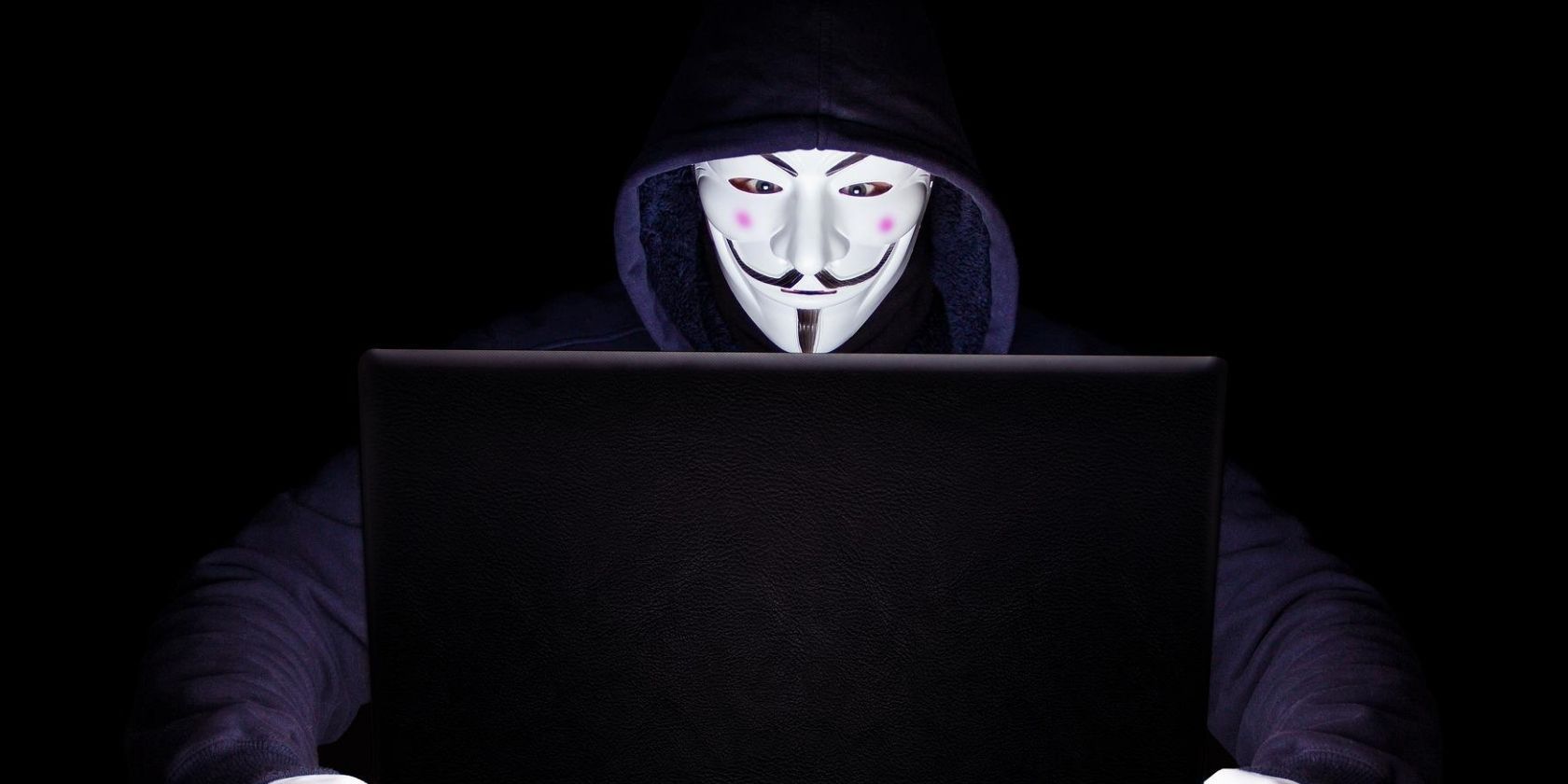hooded person in mask looking at laptop