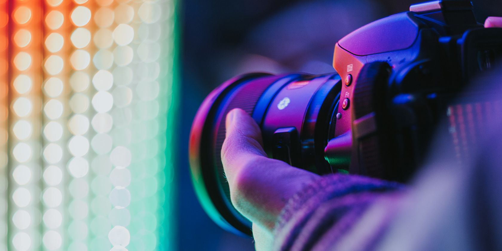 Close up of the side of a photographer's DSLR camera shrouded in purple lighting and bokeh.