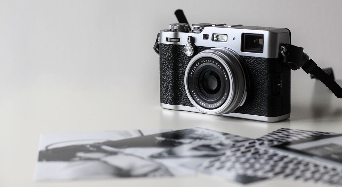 Small black film camera sat near a pile of black and white printed photos on a white table.
