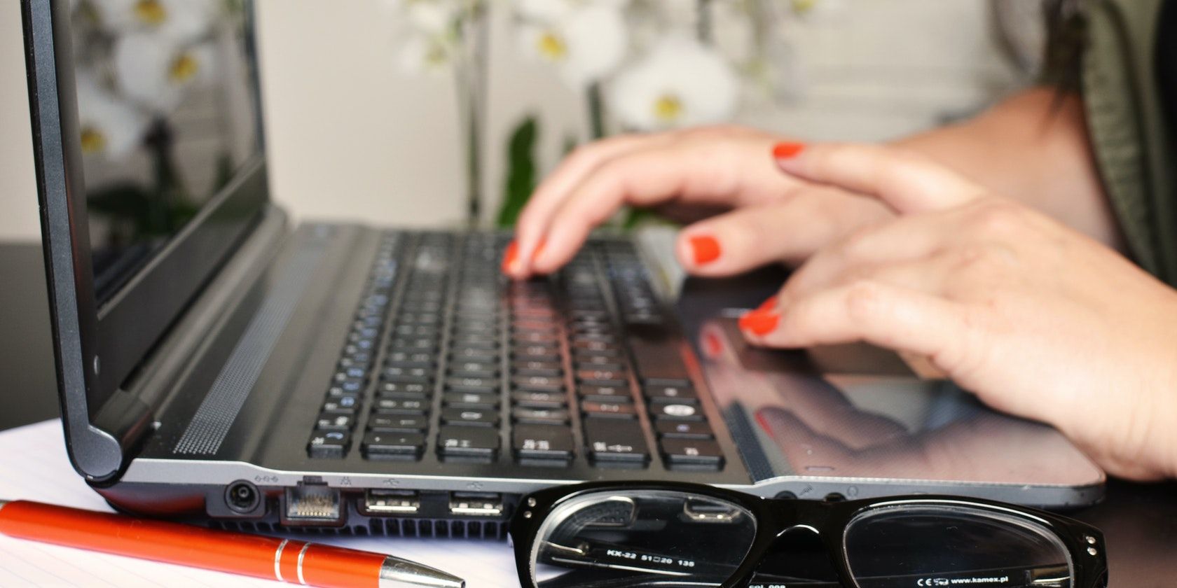 Mujer frente a una computadora portátil con un bolígrafo y gafas sobre la mesa